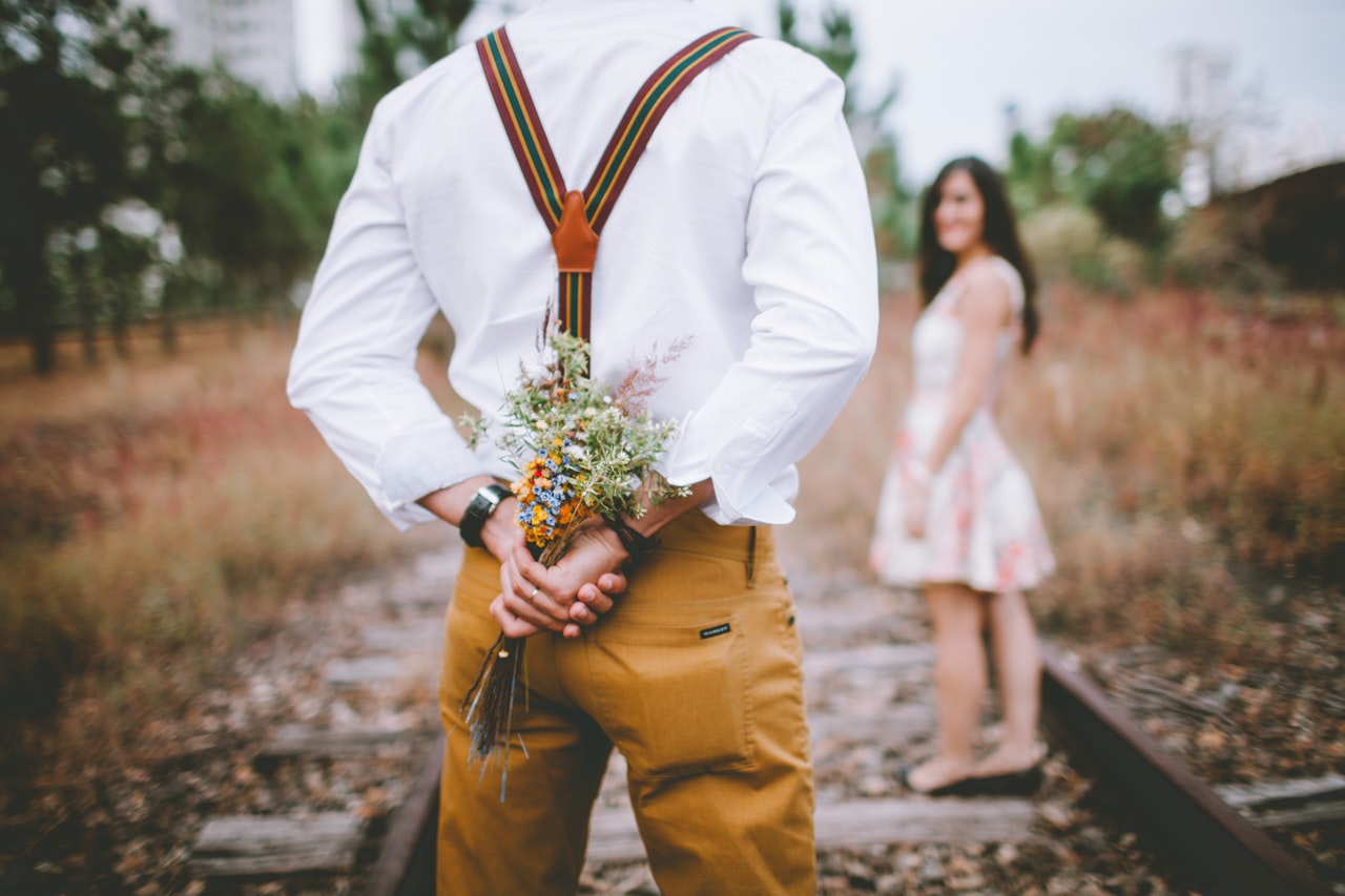 Mężczyzna trzyma w dłniach bukiet kwiatów dla kobiety