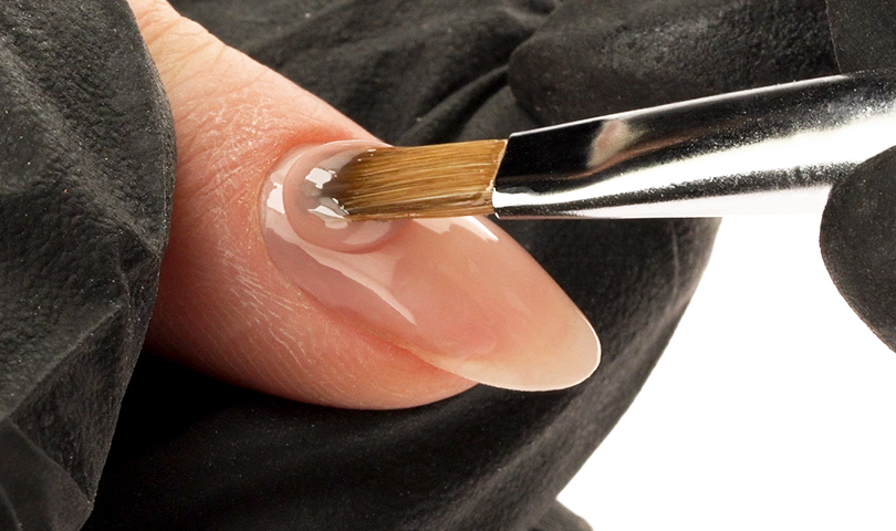 Kosmetyczka nakłada baze hybrydową na płytkę paznokcia