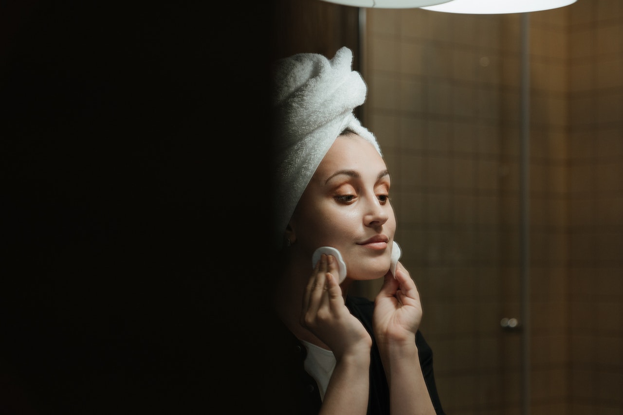 Kobieta zmywa makijaż z twarzy kosmetykami przed lustrem