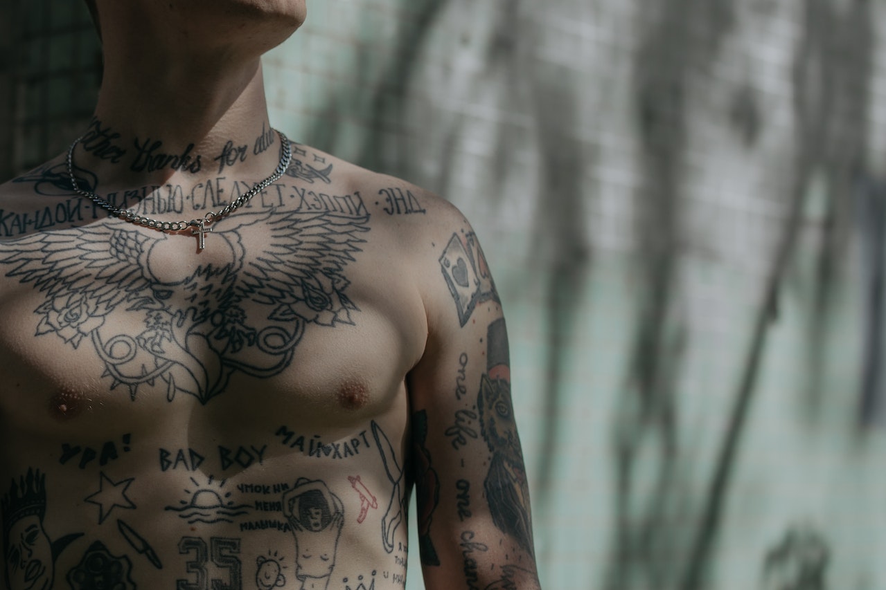 Na tej ilustracji ukazuje się mężczyzna, którego skóra zdobi klasyczny tatuaż. Wzór ten odzwierciedla tradycyjne motywy charakterystyczne dla historii tatuażu, takie jak kotwice, żagle czy serca, tworząc efekt retro i nostalgii. Ten artystyczny dodatek podkreśla indywidualność i wyrazistość jego wyglądu, jednocześnie odwołując się do korzeni i historii tatuażu jako formy sztuki ciała