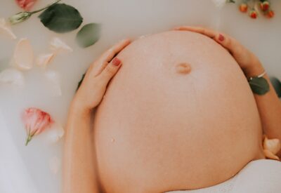 Na tym obrazku możemy dostrzec piękną kobietę w zaawansowanej ciąży. Jej delikatna twarz emanuje spokojem i radością, podkreślając ten wyjątkowy etap życia. Jej ręce delikatnie spoczywają na okrągłym brzuchu, wyrażając miłość i opiekę wobec nienarodzonego dziecka