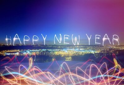 Na tym malowniczym obrazku widoczne są jasne i kolorowe fajerwerki, które rozbłyskują na nocnym niebie, tworząc magiczną iluminację. W centrum uwagi znajduje się napis "Happy New Year", który jest efektownie podświetlony i dodaje uroku tej noworocznej chwili. To widok, który kojarzy się z radosnymi obchodami nocy sylwestrowej i początkiem nowego roku, pełnego nadziei i optymizmu